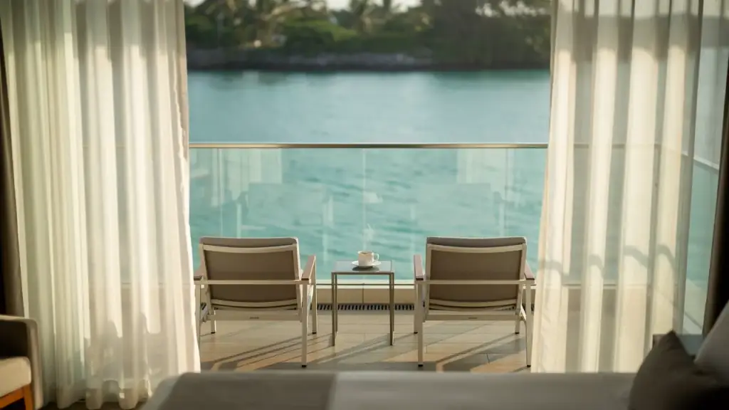 A resort balcony with two lounge chairs and a coffee cup above a turquoise lagoon